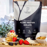 Pure Plant Protein package with a stack of pancakes, berries, and granola on a table.